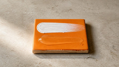 An opaque white mineral cream swipe and a clear gel swipe side by side on an orange tile, showing zinc oxide versus zinc PCA